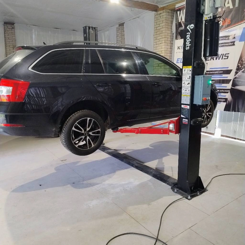 Czarne kombi uniesione na podnośniku w nowoczesnym warsztacie samochodowym.