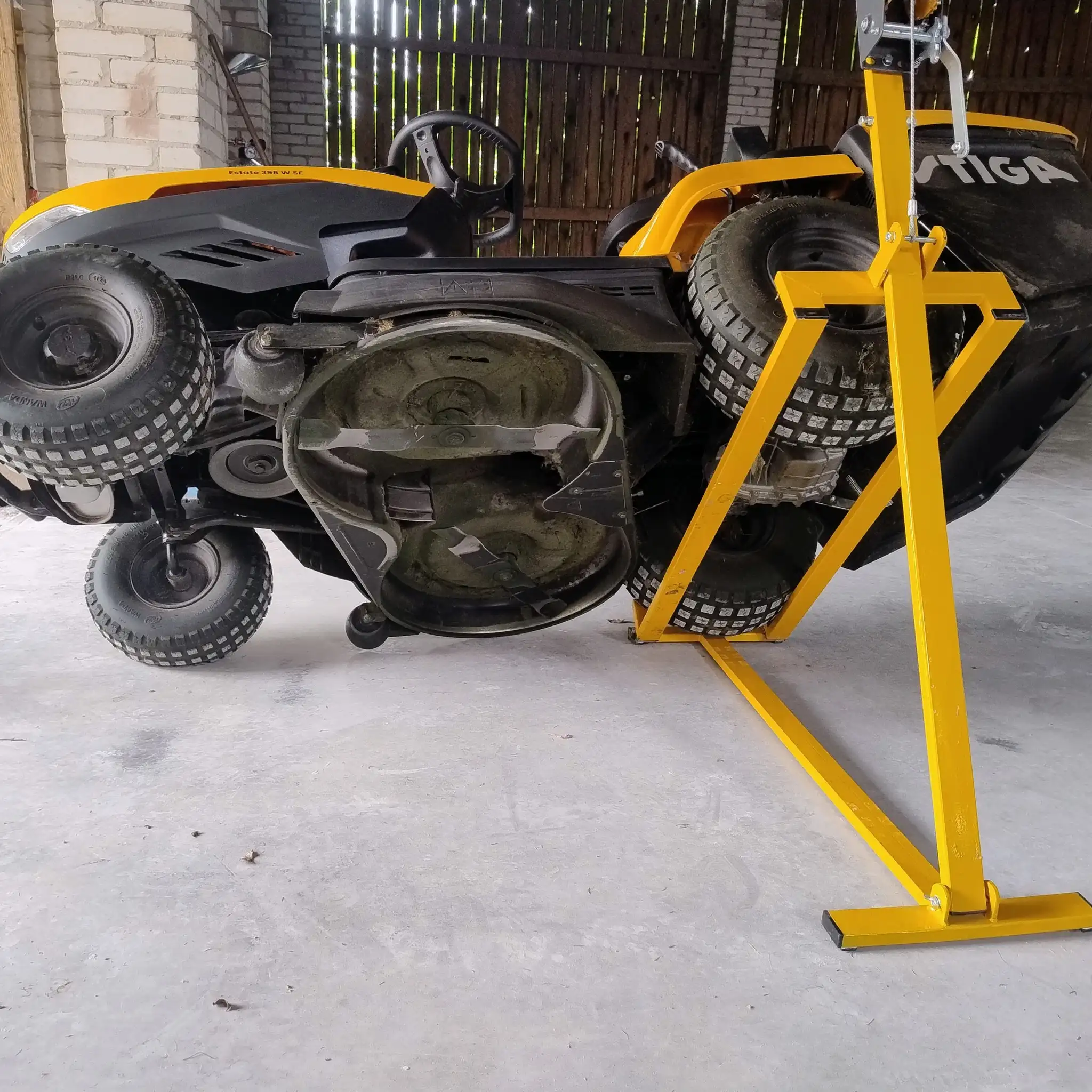 Traktorek ogrodowy ustawiony na boku na żółtym stojaku serwisowym.